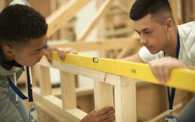 Two male college students using spirit level on frame in woodworking workshop